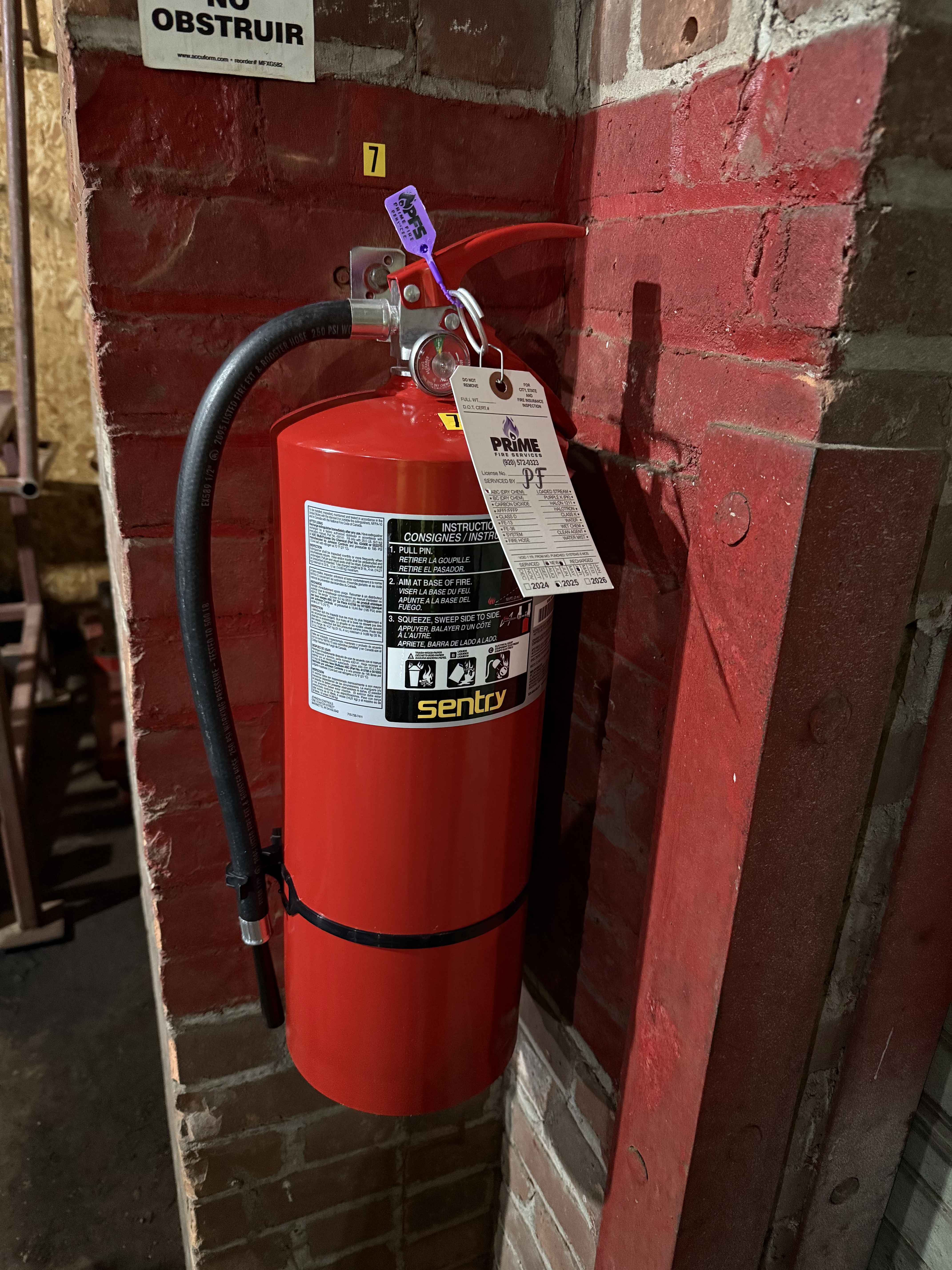 Fire extinguisher with Prime Fire Services inspection tag mounted on wall